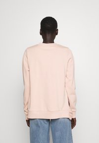 Lichtroze sweatshirt met een ronde hals, zachte textuur, ribgebreide manchetten en zoom, gecombineerd met lichtblauwe jeans. Gezien vanuit de achterkant.