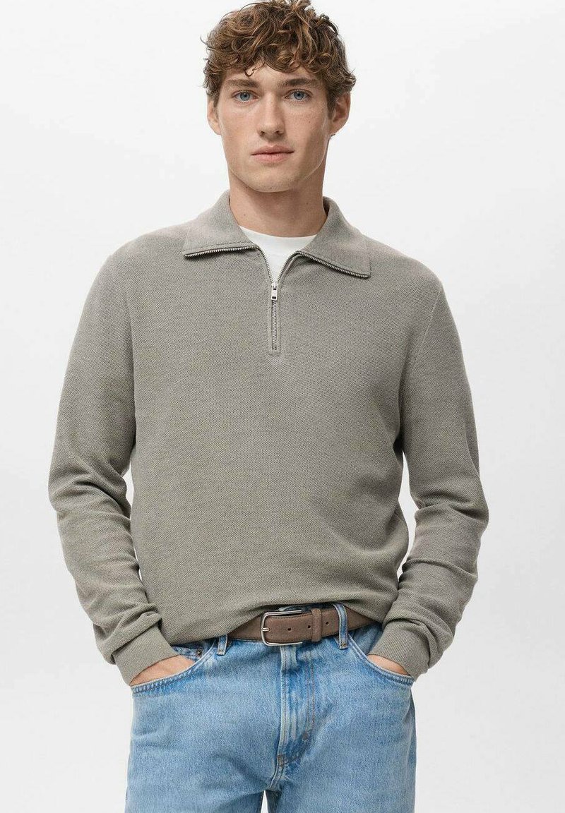 Maglione a maglia grigio chiaro con zip e colletto, caratterizzato da un motivo strutturato, abbinato a jeans azzurri slavati e cintura marrone.
