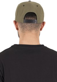 Cappellino da baseball verde oliva con cinturino regolabile in plastica nera sul retro, indossato sopra una maglietta scura, focalizzandosi sulla texture e sulla forma del cappello.