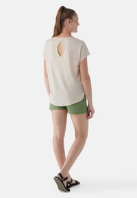 Beige kortærmet top med en nøglehulsvending bagpå, parret med grønne shorts og sorte sandaler. Glat tekstur, afslappet pasform.