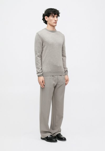 Pulôver cinza de malha com gola redonda, combinado com calças cinzas claras. O conjunto apresenta uma textura suave e um corte descontraído, complementado por sapatos pretos.