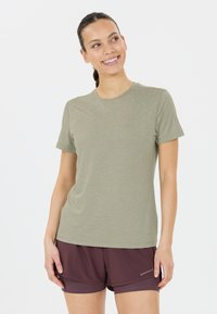 Camiseta de manga corta en un verde oliva apagado, con un clásico cuello redondo y una tela suave y ligera. Llevada con pantalones cortos de color marrón oscuro.