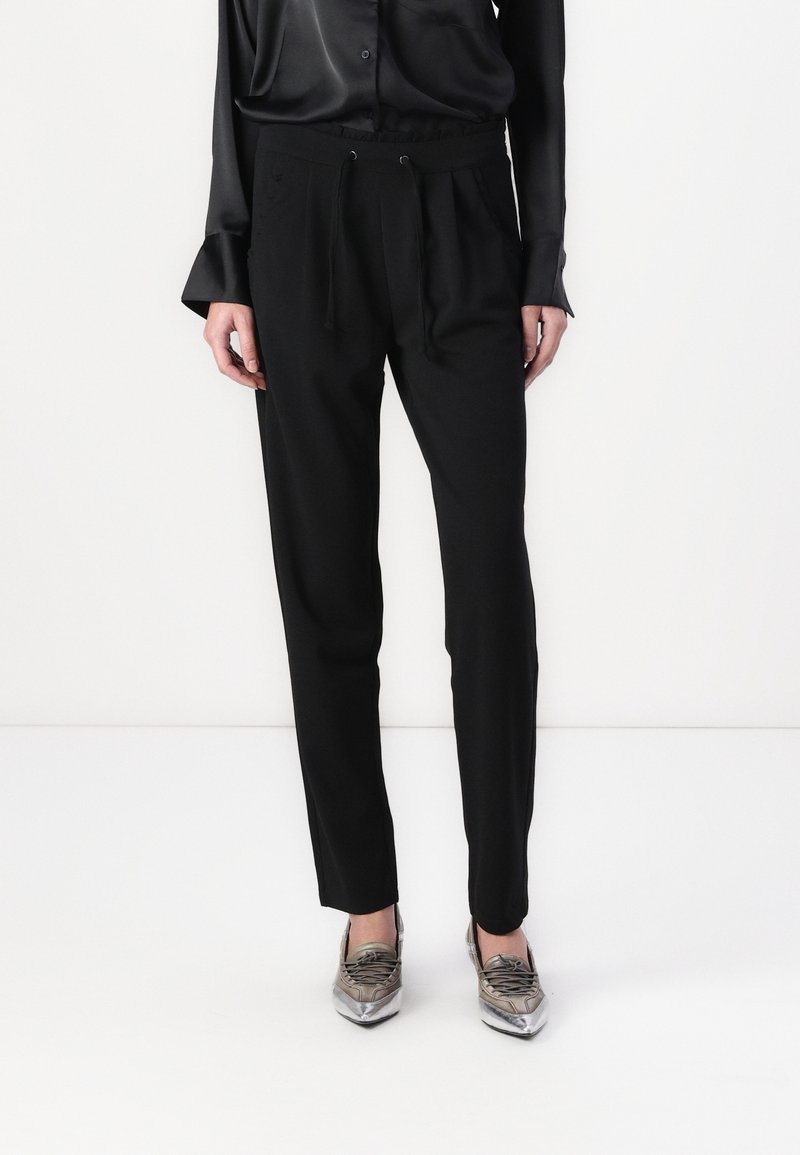 Svarta byxor med dragsko i midjan, slim fit och sidofickor. Pairade med en blank svart blus och metalliska skor.