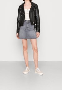 Veste de motard en cuir noir, débardeur blanc, mini-jupe en jean gris à ourlet effiloché, et baskets beige avec accents gris.