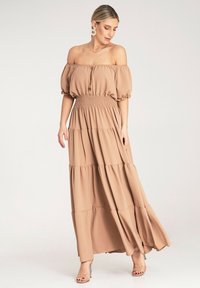 Sukienka maxi z odkrytymi ramionami, warstwowa, w jasnym beżu, z gumką w pasie i krótkimi bufkami; zdobiona drewnianymi guzikami z przodu.
