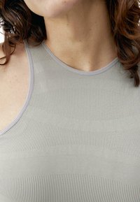 Šviesiai pilkas sportinis tanktopas, pagamintas iš tekstūruoto ripsinio audinio su pakaitomis lygiomis ir griovelinėmis raštomis bei apvaliu iškirpimu.