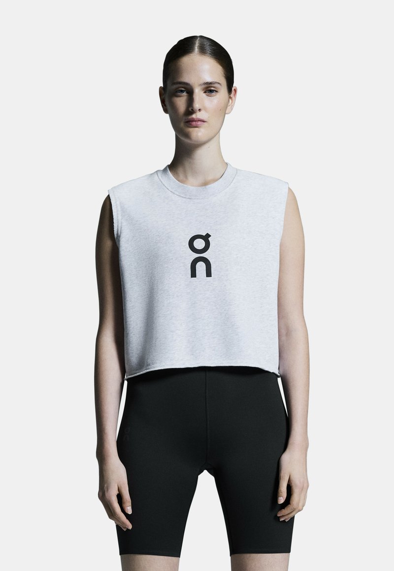 Gekürztes graues ärmelloses Oberteil mit einem schwarzen Grafiklogo auf der Vorderseite, kombiniert mit enganliegenden schwarzen Shorts. Glatte Stofftextur.