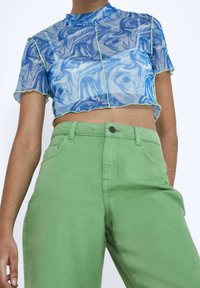 Cropped top trasparente con motivo marmorizzato blu e maniche corte, abbinato a pantaloni a vita alta verde chiaro con chiusura a bottone.
