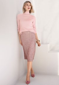 Lichtroze coltrui, rosegouden glinsterende midi-rok en roze hakken met vierkante accenten. De achtergrond is eenvoudig en wit.