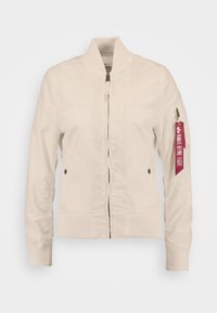 Veste bomber beige clair en tissu lisse, dotée d'un col et de poignets côtelés, d'une fermeture éclair à l'avant et d'une poche à fermeture éclair sur la manche avec une étiquette rouge.