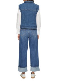 Denim vest en spijkerbroek met wijde pijpen, beide in donkerblauw. Het vest heeft een kraag en is mouwloos. De jeans hebben een omgeslagen zoom en vijf zakken.