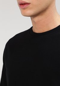 Svart sweatshirt med rund hals och ribbade muddarmar. Mjuk textur och avslappnad passform. Inga synliga m önster eller logotyper.