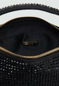 Bolso de mano negro con un exterior texturizado y adornos metálicos, cierre de cremallera y un forro interior suave con una etiqueta de la marca.