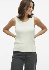 Top de color verde claro, sin mangas, con un escote redondeado y textura de canalé. Combinado con pantalones de mezclilla oscuros. Diseño sencillo y moderno.