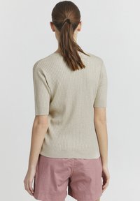 Maglione a coste beige con maniche corte, design aderente e lavorazione a maglia testurizzata. Indossato con pantaloni corti rosa chiaro per un contrasto.