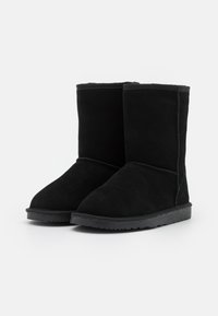 Black suede ankle boots with a rounded toe, flat rubber sole, and soft interior lining, featuring stitched seams along the sides.