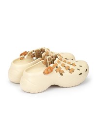 Zuecos de color crema con un diseño texturizado, acentos en tono marrón y agujeros cortados para ventilación. Presentan correas ajustables para un ajuste seguro.
