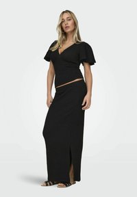Conjunto negro de dos piezas que presenta un top envolvente texturizado con mangas acampanadas y una falda larga con una abertura lateral. Combinado con sandalias planas negras.