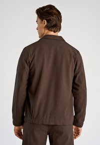 Bruine jas met een kraag, elastische zoom en een gladde textuur, gezien van achteren. Eenvoudig ontwerp met minimale details.