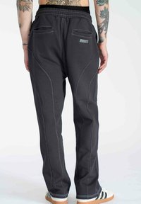 Black sweatpants with white stitching detail, elastic waistband, and two back pockets. Features tapered legs and a smooth fabric texture.