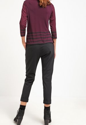 Bordeauxfarbenes Oberteil mit drei Viertelärmeln und schwarzen Streifen, kombiniert mit schwarzen, schmal zulaufenden Hosen. Stiefel mit einem kleinen Absatz runden das Outfit ab.