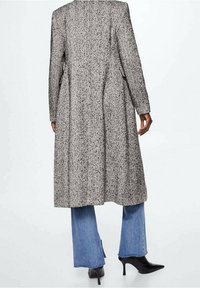 Lange grijs-zwart gespikkelde jas met een rechte snit, voorzien van zijzakken en een gladde textuur, gedragen over uitlopende blauwe denim jeans.