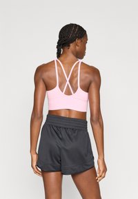 Jasnoróżowy sportowy biustonosz z konstrukcją na kształt litery X na plecach, zestawiony z czarnymi szortami sportowymi z marszczonym pasem i gładką teksturą.