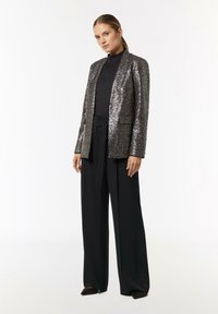Sequin blazer in silver and black, slim fit with a notch lapel, paired with high-waisted black trousers; smooth texture and shiny detail.