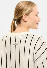 Sweter z dzianiny w pionowe czarne paski na beżowym tle, z metką z napisem "JOHNNY URBAN" z tyłu przy dekolcie.