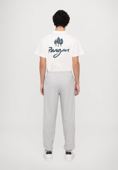 Hvid t-shirt med grønt "Pangaia" logo på ryggen, parret med grå sweatpants med elastisk talje og opkrøllede kanter.