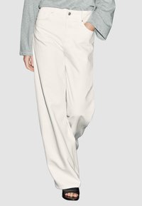 Pantaloni bianchi a gamba larga realizzati in denim, con chiusura frontale a bottone, due tasche laterali e una finitura liscia e non testurizzata.