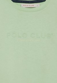 Camiseta de manga corta verde claro con cuello redondo. Presenta el texto troquelado "POLO CLUB" y "ESTABLECIDO EN 2012" en color contrastante.
