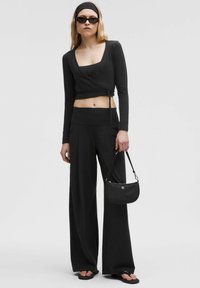 Un crop top noir à manches longues, un pantalon large noir taille haute et un petit sac à bandoulière noir. Les accessoires incluent des lunettes de soleil élégantes.