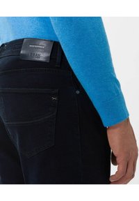 Dark blue jeans with a leather tag, overviewing the back pocket. A textured, fitted blue sweater is partially visible on the upper arm.