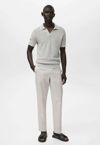 Polo à manches courtes gris clair côtelé avec un col plat, associé à un pantalon beige pâle et des sandales noires. Design simple et palette de couleurs monochromatique.