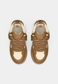 Brune suedelær og kremfarget skinn sneaker med tykk såle, hvite lisser og en teksturert bakside. Har merkevaren logo på tungen og siden.