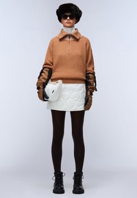 Bruine gebreide trui met ritssluiting aan de kraag, witte gewatteerde mini rok, bruine handschoenen, zwarte panty en stevige zwarte laarzen. Accessoires zijn onder andere een zonnebril en een bonten hoed.