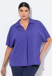 Lila kurzärmlige Bluse mit Kragen, die eine Faltenlegung an der Brust aufweist, aus einem glatten Stoff gefertigt und mit einem lockeren Schnitt.