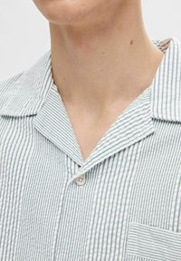 Koszula z krótkim rękawem, z kołnierzykiem, w jasnoniebieskie i białe pionowe paski, z naszywaną kieszenią i jednym guzikiem, wykonana z teksturowanej tkaniny.