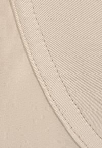 Beiger Stoff mit einer strukturierten Oberfläche, der eine auffällige Naht aufweist. Das Material wirkt weich mit feinen Rippungen und ordentlichen Nähdetails.