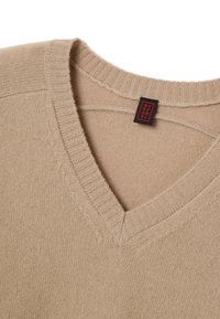 Beige V-hals trui gemaakt van zachte gebreide stof; heeft een ribbelboord bij de hals en stikdetails. Label zichtbaar aan de bovenkant, dat het merk aangeeft.