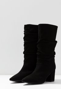 Czarne, luźne botki za kostkę wykonane z miękkiego materiału, z wąskim noskiem i grubym obcasem, z marszczoną teksturą wzdłuż cholewki.