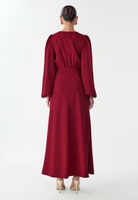 Pikk bordoopunane kleit puhvis varrukate, vöökoha kokkusurutise, taga lukuga ja voolava seelikuga; kombineeritud nude värvi kontsadega.