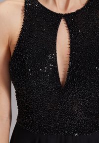 Schwarzes, mit Pailletten besetztes Kleid mit hohem Kragen, tiefem Schlüsselloch-Ausschnitt und einem glatten, fließenden Rock. Textur und Details sind im Oberteil deutlich erkennbar.