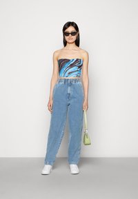 Top cropped azul e preto sem alças, jeans de ganga de cintura alta azul claro, sapatilhas brancas e uma pequena mala verde.