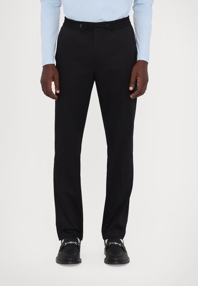 Black elastic waistband trousers with a straight leg design, made from smooth fabric, worn with black shoes featuring decorative hardware accents.