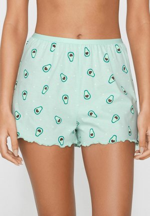 Femme portant un short vert clair avec un imprimé avocat et un ourlet festonné, dévoilant le ventre et le haut des cuisses.