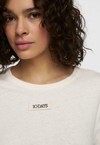 Witte katoenen t-shirt met een ronde halslijn, voorzien van een klein zwart geborduurd label met de tekst "10 DAYS" op de voorkant. Geweven stof.