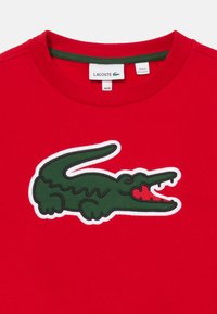 Camisa roja Lacoste con logo de cocodrilo verde y cuello acanalado, tamaño 4A/4, fabricada en Sri Lanka.