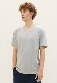 Camiseta de algodón gris con cuello en V, de mangas cortas, ajuste relajado y textura suave, combinada con pantalones azul marino sobre un fondo neutro.